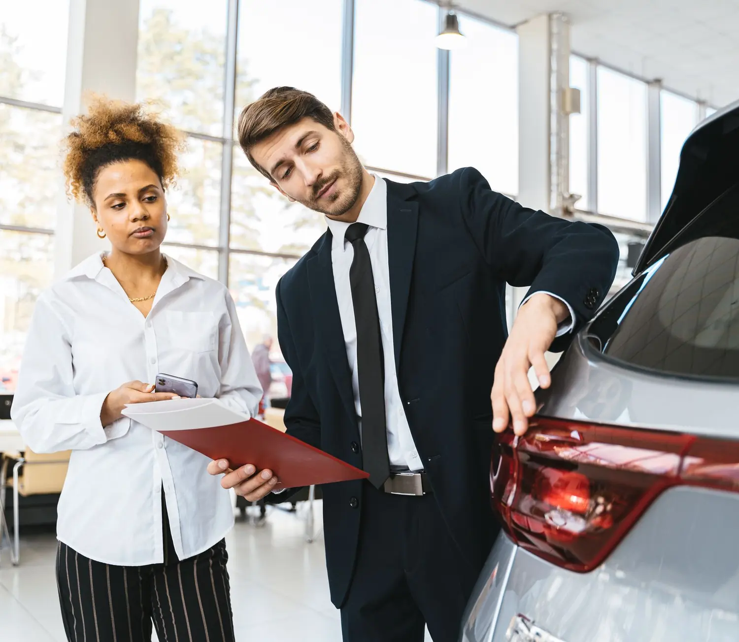 Verkäufer zeigt einer Kundin ein Auto im Autohaus
