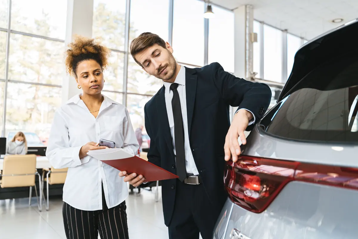 Verkäufer zeigt einer Kundin ein Auto im Autohaus